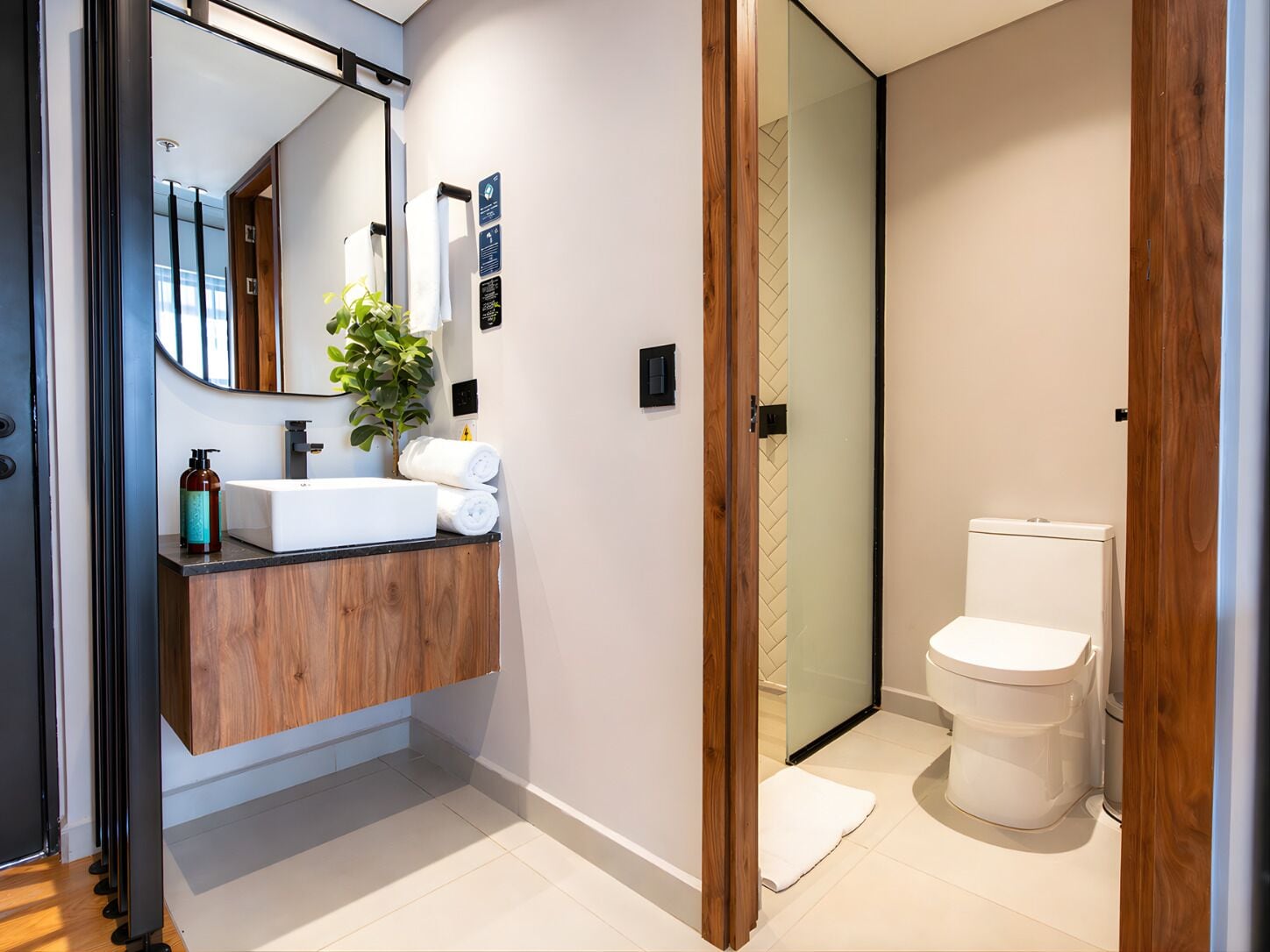 A modern bathroom with a wooden vanity, a mirror, a plant, and a toilet.