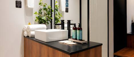 Ein modernes Badezimmer mit Waschtisch aus Holz, weißem Waschbecken und zwei Shampooflaschen.