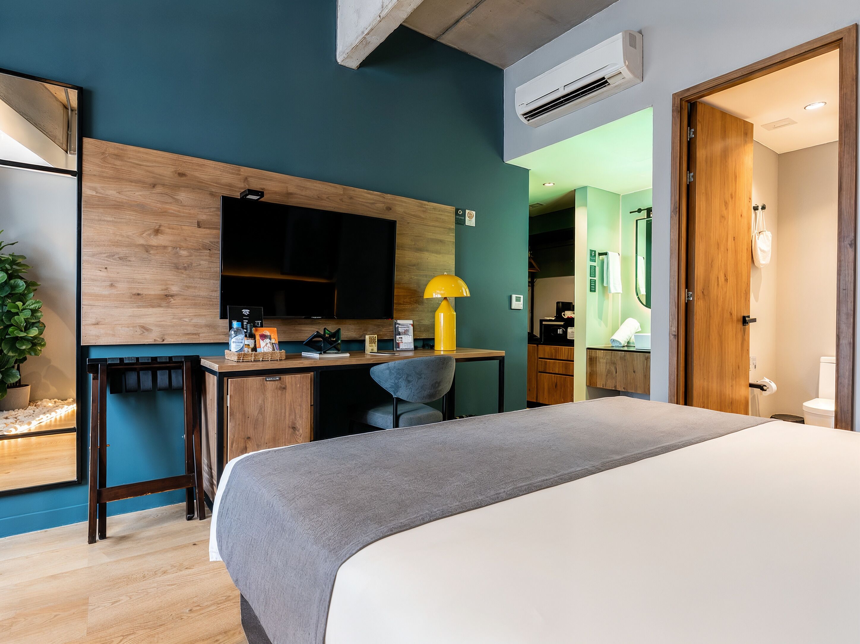 A modern hotel room with a bed, desk, and kitchenette.
