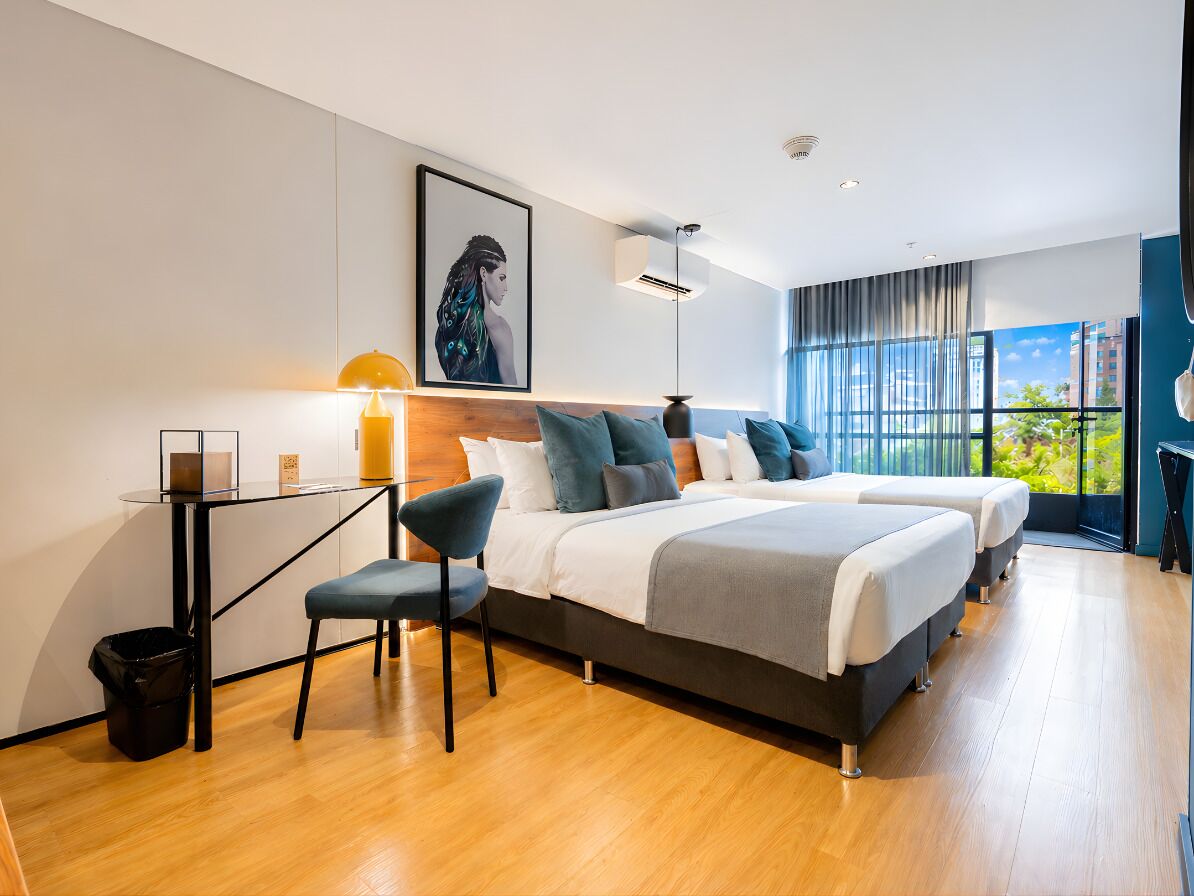 A modern hotel room with two beds, a desk, and a large window.