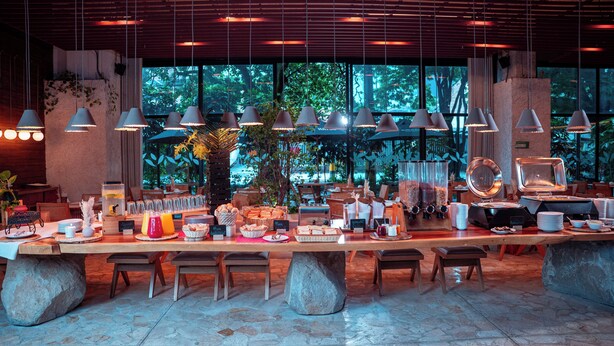 Un bufé de desayuno con una variedad de alimentos, incluyendo frutas, pasteles y bebidas, dispuesto sobre una amplia mesa con bases de piedra.