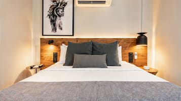 Une chambre d’hôtel moderne avec une tête de lit en bois, une œuvre d’art encadrée, un appareil de climatisation, une lampe de chevet et une table de chevet.