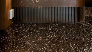 Una mesa de recepción con detalles de madera, una encimera negra y un cartel con texto escrito a mano. Hay tres lámparas colgantes sobre la mesa.