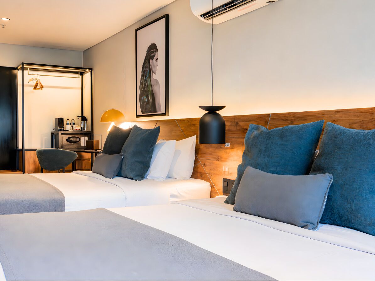 Habitación de hotel moderna con dos camas, cabecero de madera, escritorio con silla y lámpara de pared.