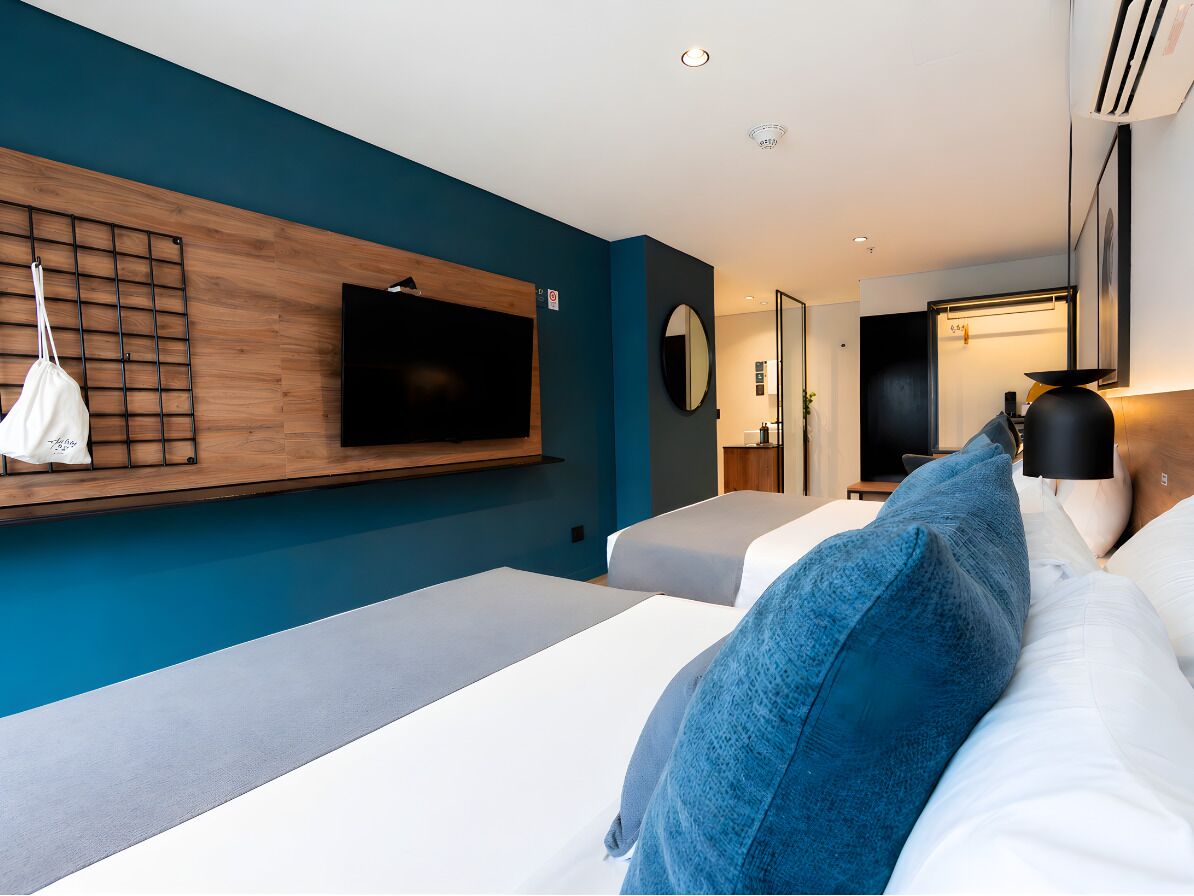 A modern hotel room with a large bed, a TV mounted on the wall, a bedside table, and a mirror.