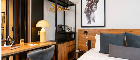 A hotel room with a bed, desk, chair, lamp, and a framed artwork on the wall.