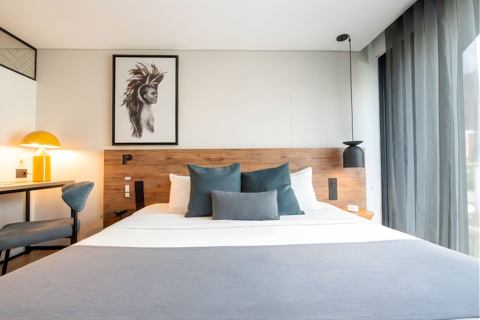 Una habitación de hotel con cama, escritorio, silla, lámpara y un cuadro en la pared.