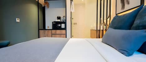 A modern hotel room with a large bed, a desk, and a bathroom visible through an open door.
