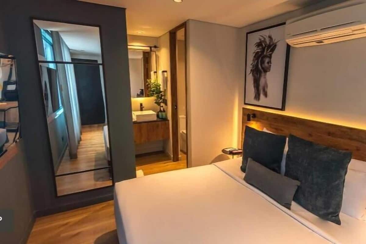 A modern hotel room with a bed, bedside table, and a large mirror.