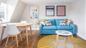 Uma sala de estar moderna com um sofá azul, uma mesa de jantar com cadeiras e um tapete amarelo.