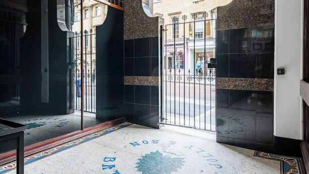 Entrada de hotel com piso ladrilhado, um portão de metal e vista para a rua.