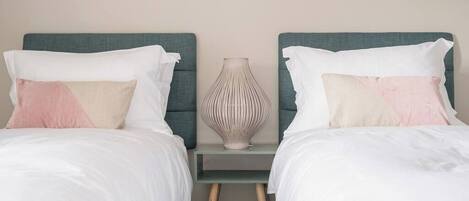 A double bed with white and pink pillows, a vase on a nightstand, and a teal headboard.
