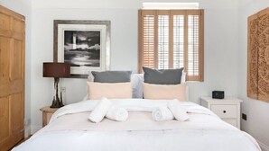 A neatly made bed with white linens and rolled towels, a framed black and white photograph on the wall, a wooden door, and a window with wooden blinds. - Murphy's House Central Townhouse W/courtyard (Bath)