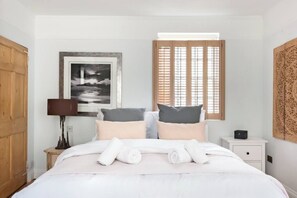 A neatly made bed with white linens and rolled towels, a framed black and white photograph on the wall, a wooden door, and a window with wooden blinds. - Murphy's House Central Townhouse W/courtyard (Bath)