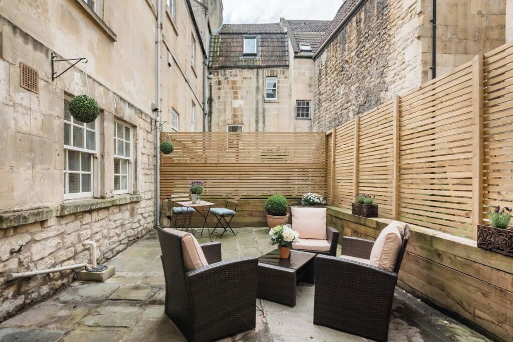 A courtyard with wicker furniture, potted plants, and a wooden fence.