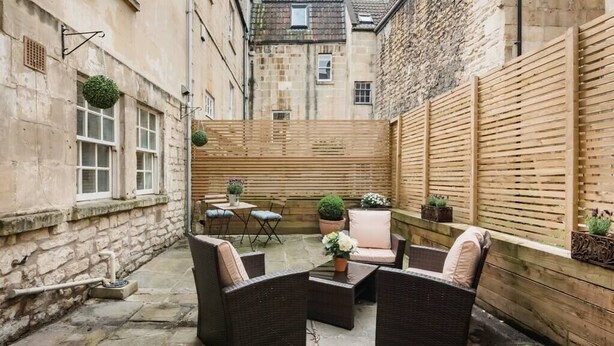 A courtyard with wicker furniture, potted plants, and a wooden fence. - Murphy's House Central Townhouse W/courtyard (Bath)