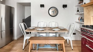 A modern kitchen with a dining table set for four, white chairs, a red stove, and a wall-mounted clock. - Murphy's House Central Townhouse W/courtyard (Bath)