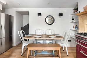 A modern kitchen with a dining table set for four, white chairs, a red stove, and a wall-mounted clock. - Murphy's House Central Townhouse W/courtyard (Bath)