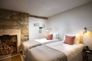 A bedroom with two beds, a stone fireplace, and a small table with a lamp. - The Courtyard - 2 bed Apt in Georgian Townhouse (Bath)