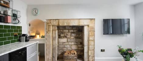 A modern kitchen with a stone fireplace, a television mounted on the wall, and a dining area with a black table.