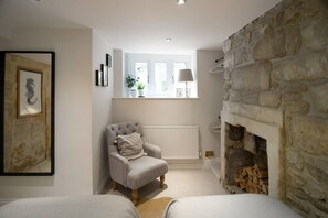 A cozy room with a stone fireplace, a comfortable armchair, a radiator, and a window with a view.
