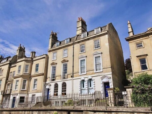 A row of traditional buildings with uniform architecture, featuring symmetrical windows and a central entrance with a decorative archway. - The Courtyard - 2 bed Apt in Georgian Townhouse (Bath)