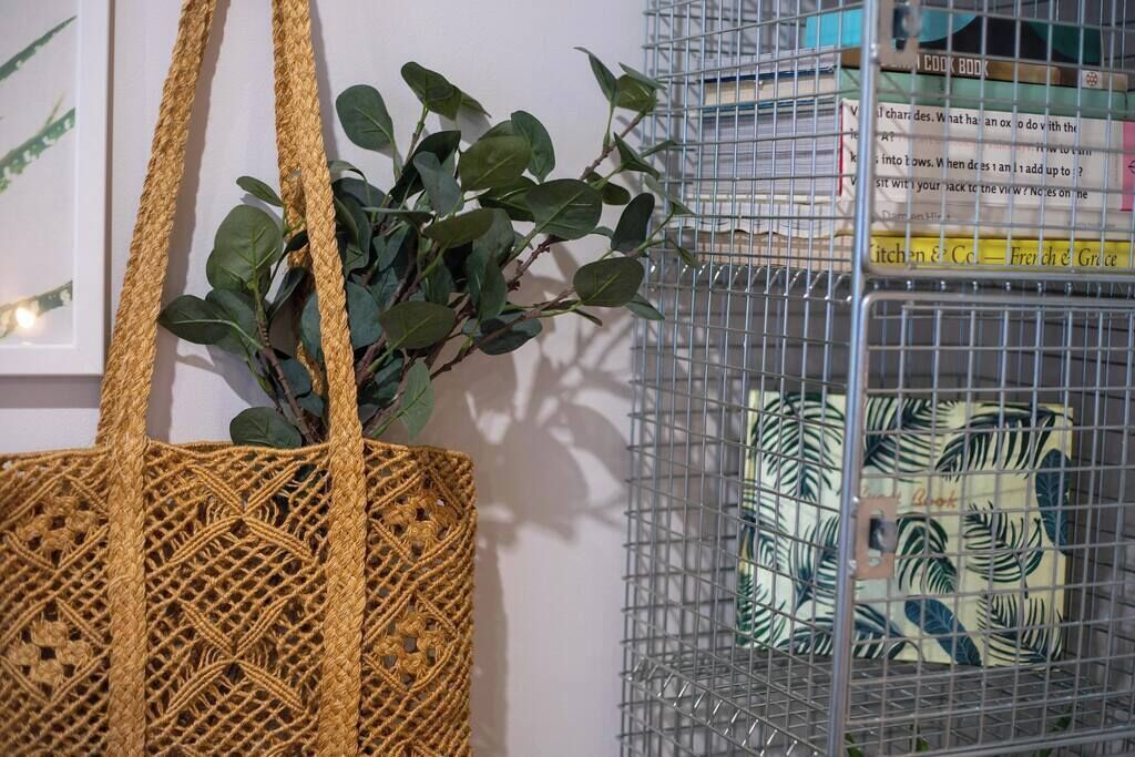 Uma bolsa de tecido, uma gaiola de metal com almofada estampada e um quadro na parede.