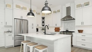 Une cuisine moderne avec des meubles blancs, un réfrigérateur en acier inoxydable, une cuisinière à gaz et deux luminaires suspendus.