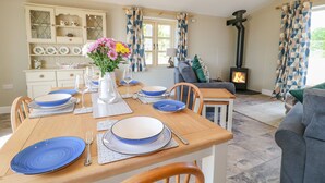 A dining area with a wooden table set for four, blue plates, and a vase of flowers. - Acorn Lodge (Stafford)