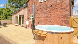 A brick building with a wooden deck, a hot tub, and a sliding glass door leading to a room. - Acorn Lodge (Stafford)
