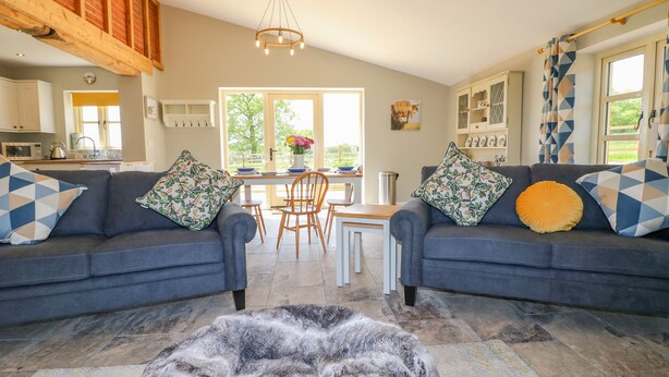 A spacious living room with two sofas, a coffee table, and a fireplace. There is a dining area with a table and chairs, and a kitchen in the background. - Acorn Lodge (Stafford)