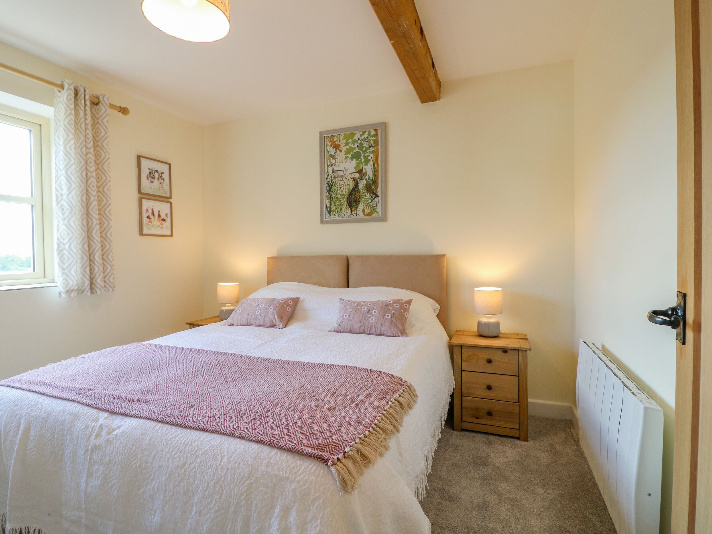 A bedroom with a large bed, two bedside tables with lamps, a radiator, and a window with curtains.