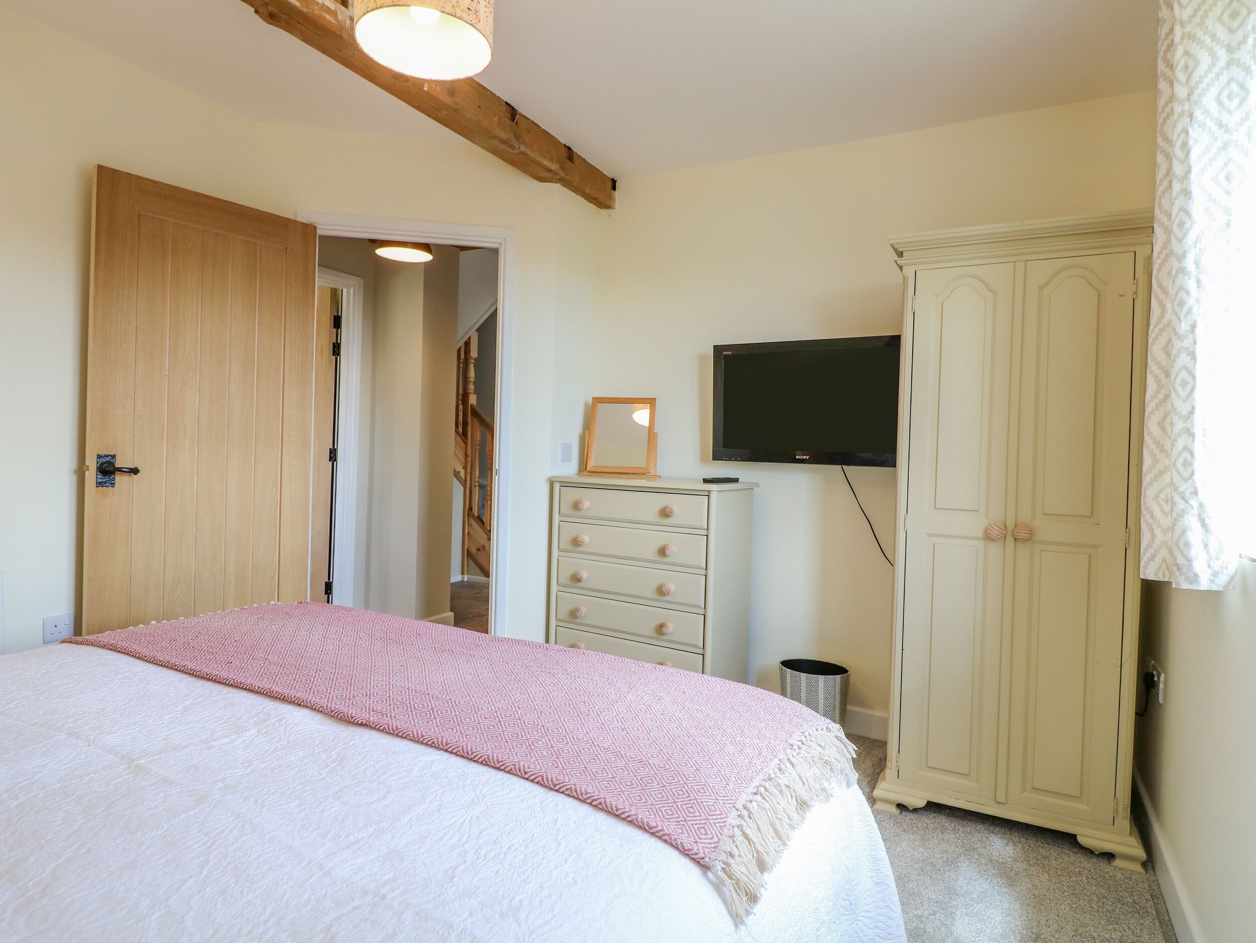 A bedroom with a bed, a wardrobe, a television, and a door leading to another room.