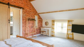 A bedroom with a sloped ceiling, a wooden bed, a desk with a chair, a mirror, and a window with curtains. - Acorn Lodge (Stafford)