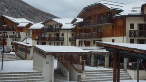 A cluster of wooden buildings with balconies, a snow-covered ground, and a mountain in the background. - 100m from resort center, 1st floor, swimming pool, sauna, balcony, tv, ski locker, 35m², Les Orres (Les Orres)