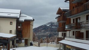 A snow-covered outdoor area with wooden buildings and a mountain in the background. - 100m from resort center, 1st floor, swimming pool, sauna, balcony, tv, ski locker, 35m², Les Orres (Les Orres)