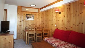A wooden-paneled room with a dining table, chairs, a sofa, and a television on a cabinet. - 100m from resort center, 1st floor, swimming pool, sauna, balcony, tv, ski locker, 35m², Les Orres (Les Orres)