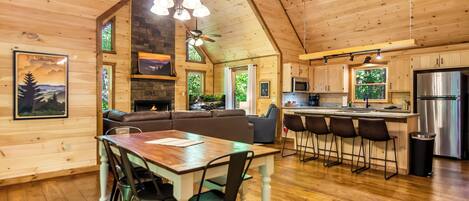 A wooden cabin interior with a dining area, kitchen, and seating.