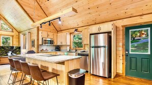 A wooden interior with a kitchen island, bar stools, stainless steel appliances, and a green door. - Spacious, New Cabin! New Hot Tub, Fire Pit, and Game Room! Dog-Friendly! (Blue Ridge)