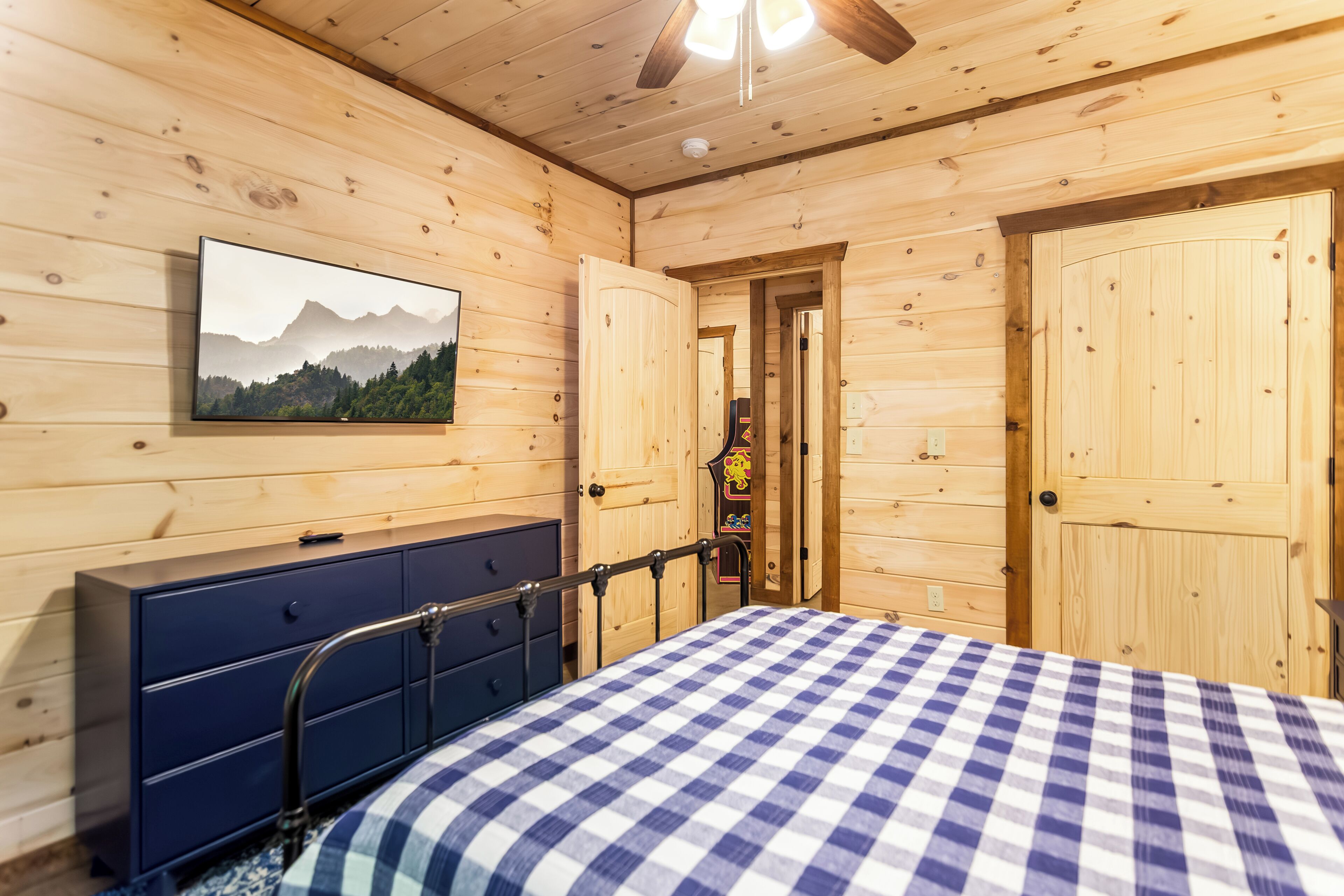 A wooden room with a bed, dresser, and a door leading to another room.