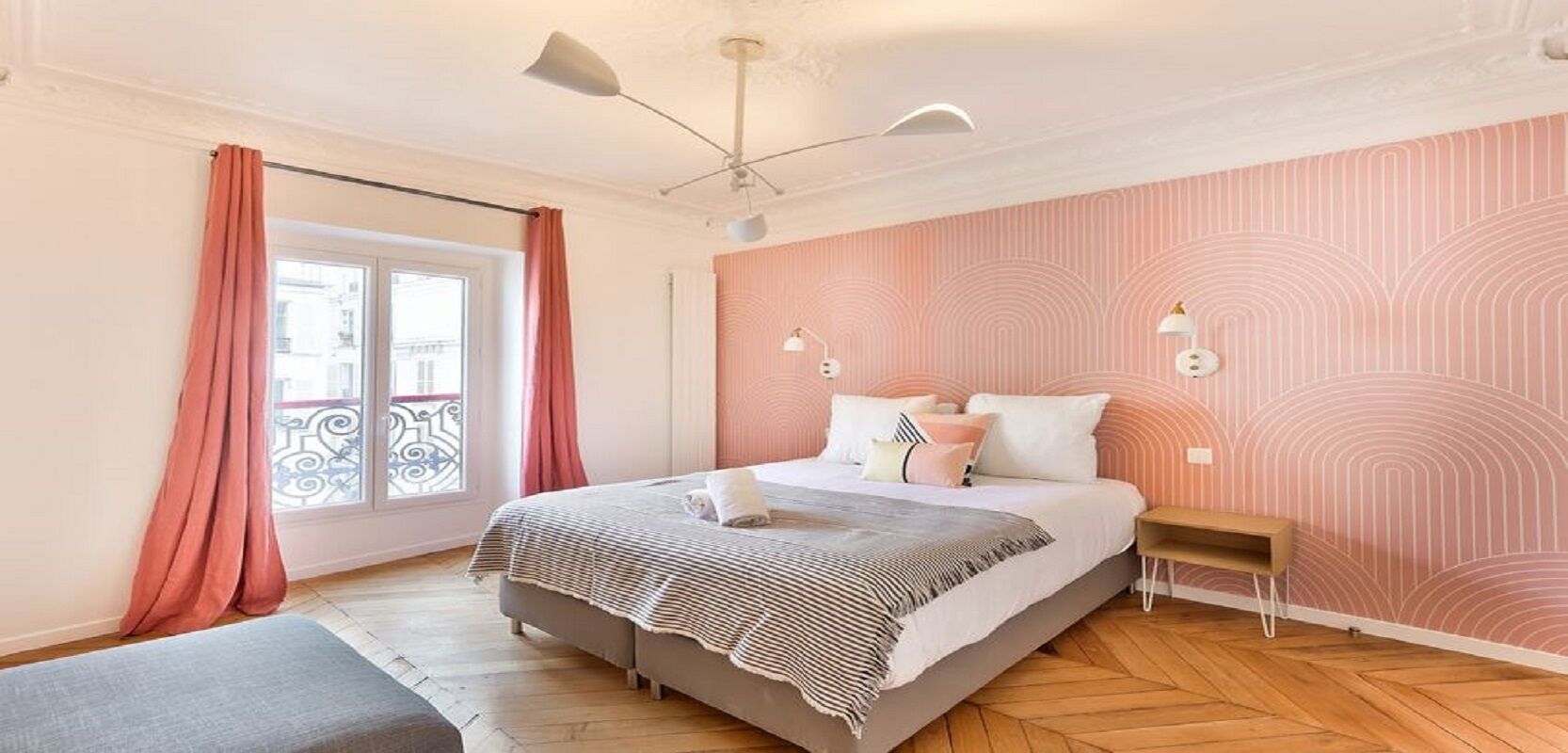 A bedroom with a bed, bedside tables, a window with curtains, and a patterned wall.