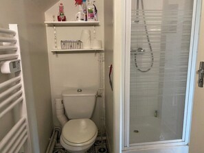 Une petite salle de bain comprenant des toilettes, un espace douche et une étagère avec des articles de toilette.