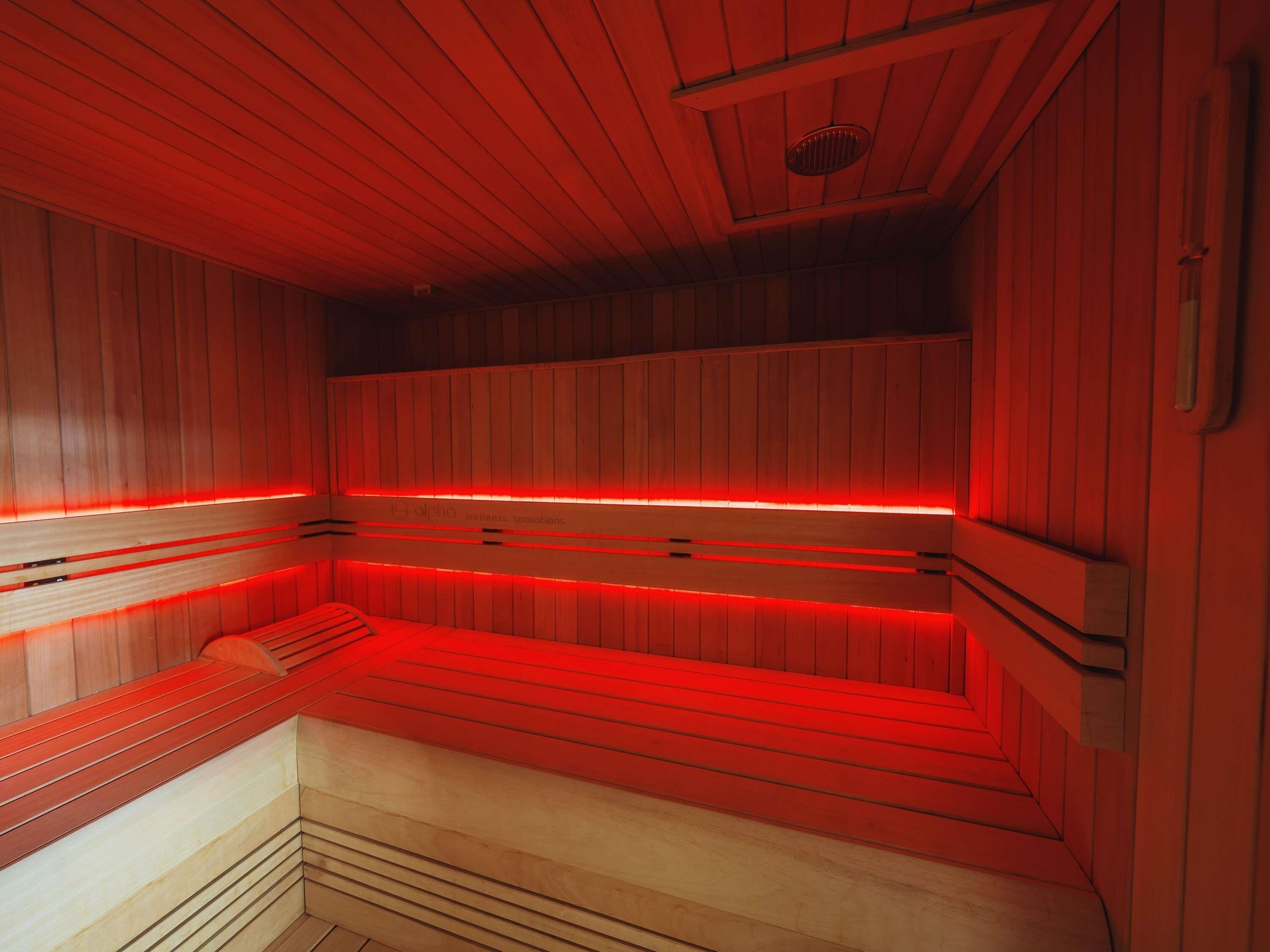 Una sauna con paredes y bancos de madera, iluminación roja y un respiradero en el techo.