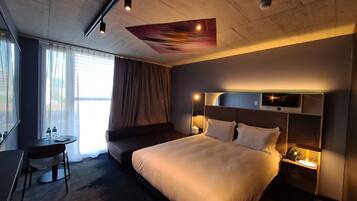 Habitación de hotel moderna con una cama grande, mesita de noche con lámpara y un escritorio con silla.