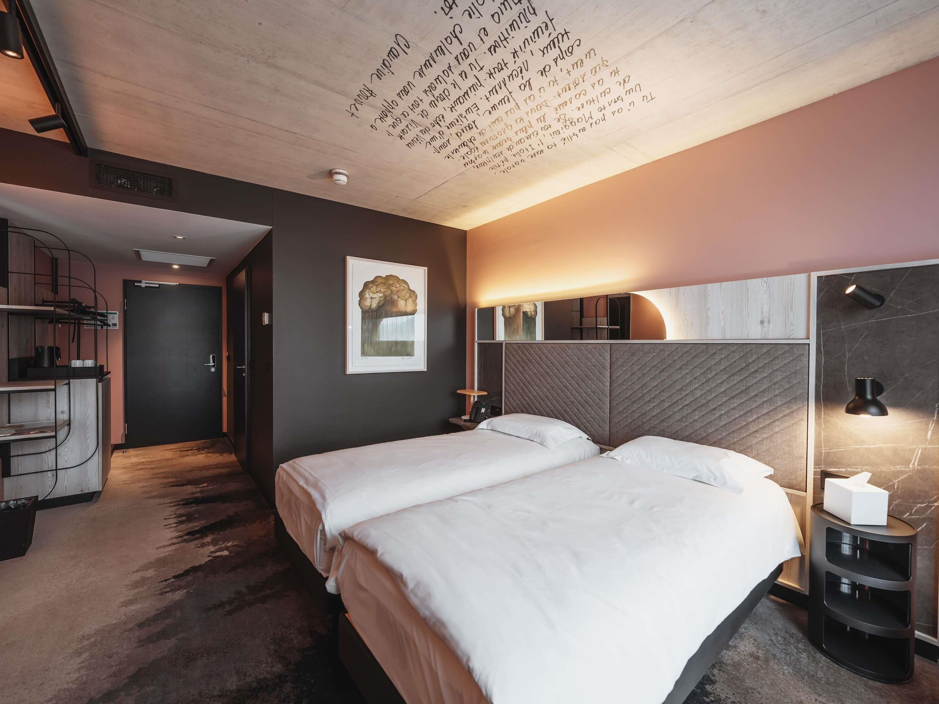 A modern hotel room with a large bed, a desk, and a mirror.