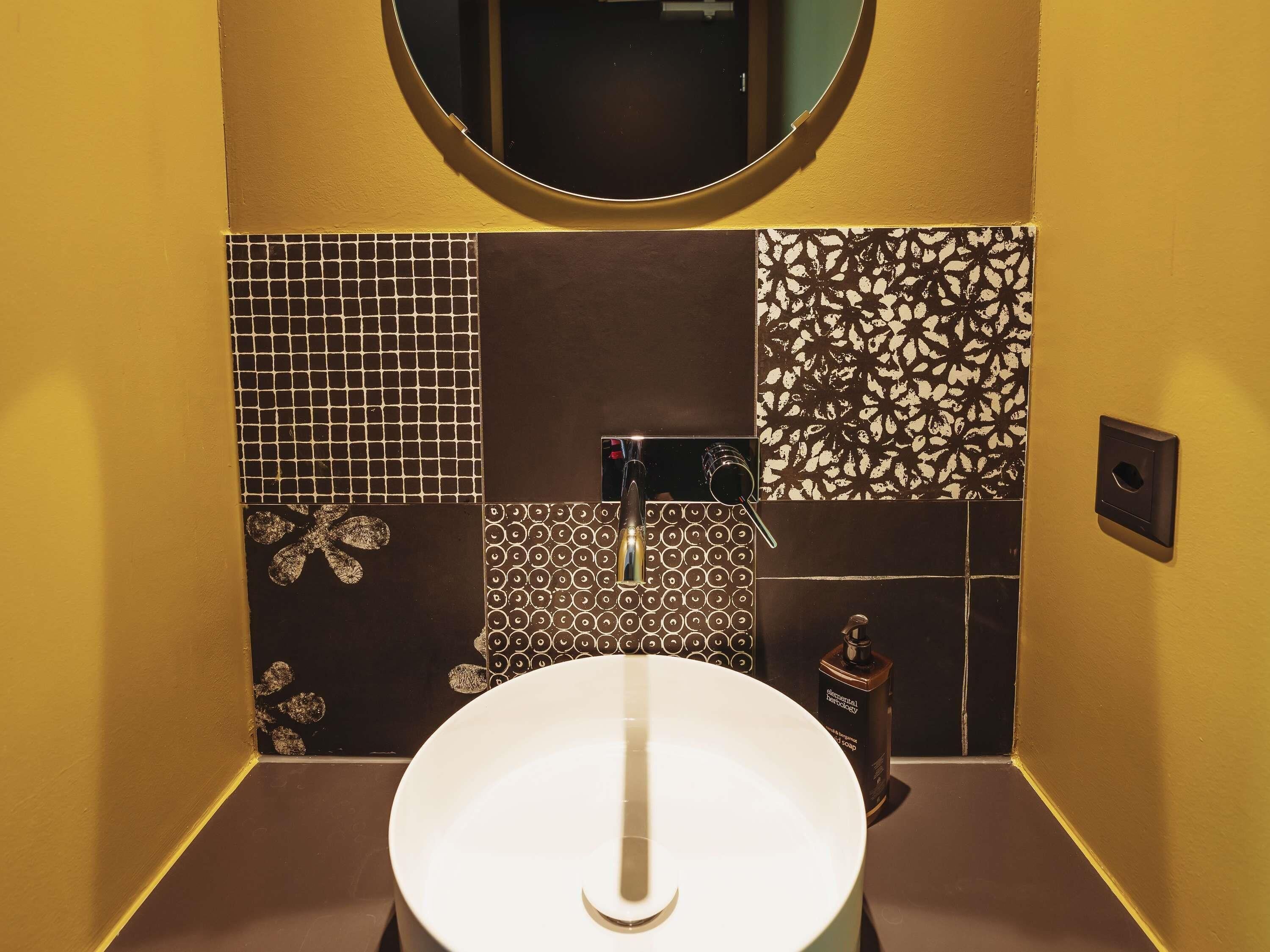 Un baño con un lavamanos blanco, un espejo encima y diversos azulejos estampados en las paredes.