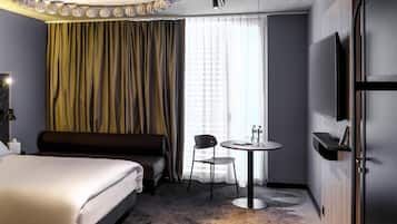 A hotel room with a bed, a desk with a chair, a TV, and a large window with curtains.