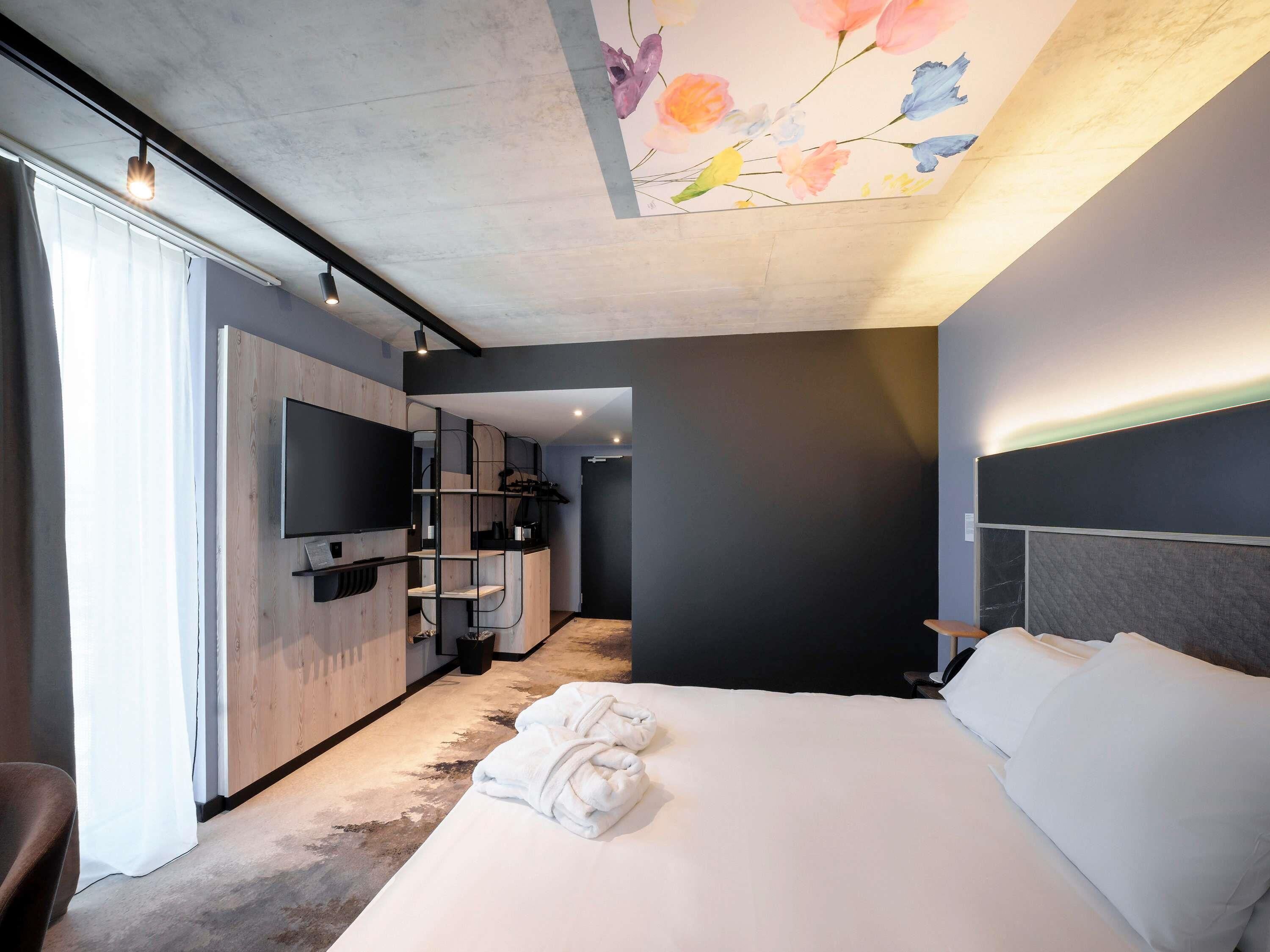 A modern hotel room with a large bed, a TV mounted on the wall, a built-in wardrobe, and a shower area.