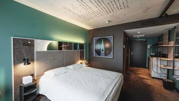 Ein modernes Hotelzimmer mit einem großen Bett, einem Schreibtisch mit Lampe, einem Wandbild und einer Treppe zu einer oberen Ebene.