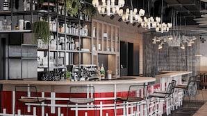 Zona de bar moderna con un diseño geométrico en la pared en tonos rojo y blanco, diversas opciones de asientos y una variedad de botellas y vasos en estanterías.
